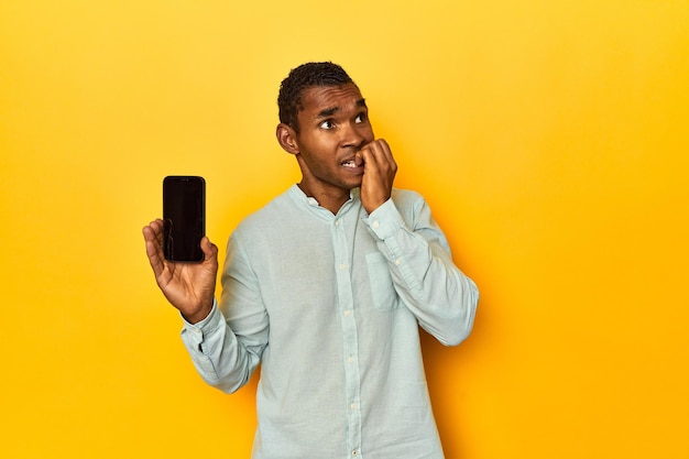African American man with mobile phone yellow studio biting fingernails nervous and very anxious