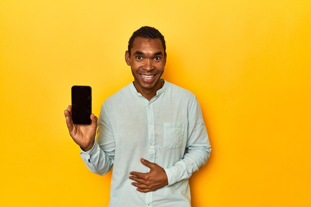 Photo african american man with mobile phone yellow studio laughing and having fun