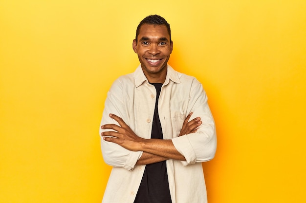 African American man with shirt yellow studio who feels confident crossing arms with determination