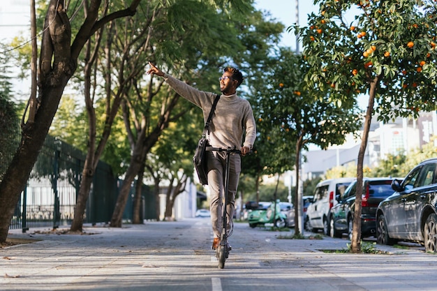 Uomo afroamericano con gilet a collo alto che si gode un giro con il suo scooter elettrico e indicando con il braccio