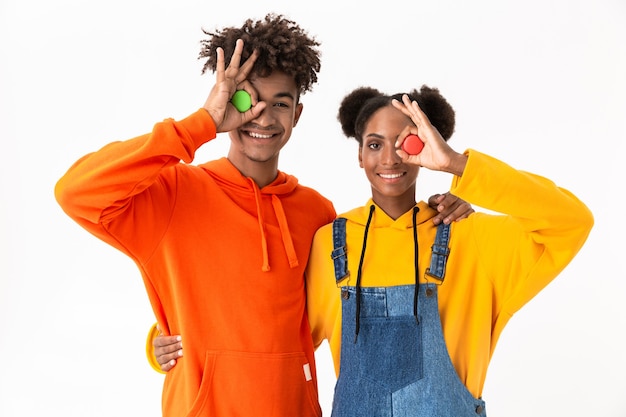 african american man and woman in colorful clothes holding macaroon biscuits, isolated over white wall