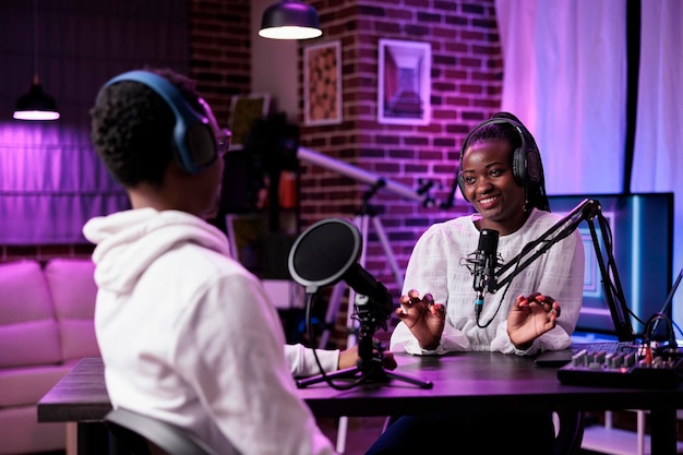 African american man and woman recording live podcast in\
studio, using sound production equipment. happy influencers meeting\
to create social media content on internet broadcast.