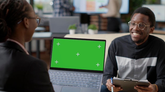 African american man and woman working together with green screen on laptop display. Business people using mockup template with isolated copy space and blank chroma key background.