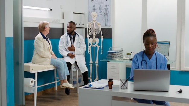 African american medic consulting senior patient in cabinet,
talking about healthcare treatment and medicine to cure disease.
woman and doctor doing checkup visit examination at clinic.