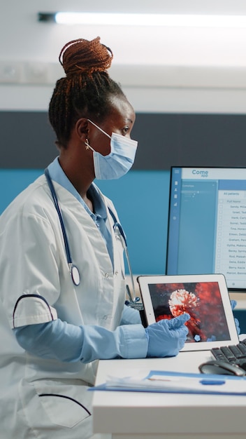 Medico e paziente afroamericano che guardano l'animazione del virus su tablet digitale indossando maschere per la protezione. medico nero che spiega i batteri e la malattia del coronavirus per la donna