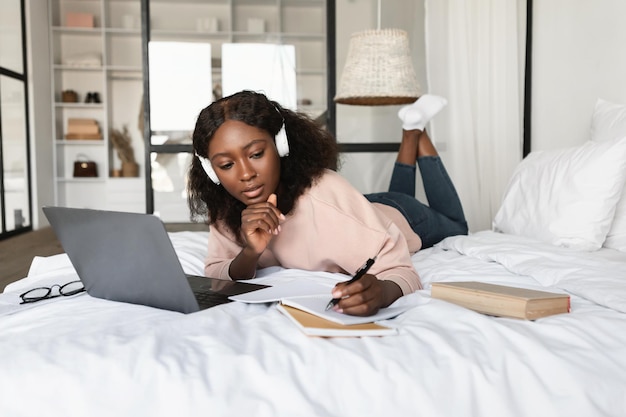African american millennial woman using laptop taking notes at home