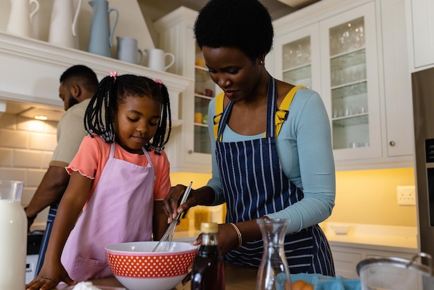 African american mother and daughter mixing batter in bowl on table in kitchen. Unaltered, lifestyle, family, love, togetherness, childhood, food, preparation and learning concept.