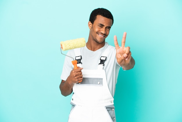 African American painter man over isolated blue background smiling and showing victory sign