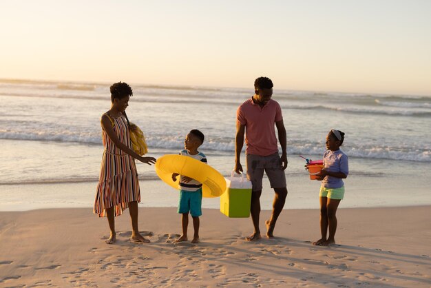 African american parents looking at son and daughter playing with inflatable ring and pail on beach