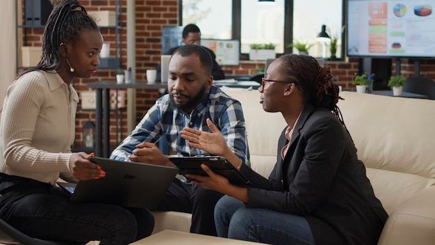 African american people meeting to plan research project in company office, analyzing statistics on digital tablet and laptop. Business partners using financial charts to work on presentation.