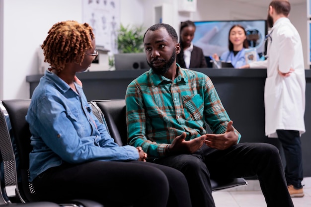 African american people talking in waiting area lobby, having medical appointment with specialist. Patients sitting in waiting room to attend healthcare checkup visit, facility.