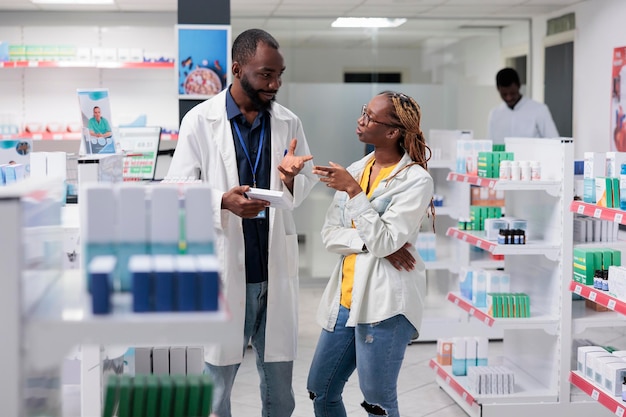 African american pharmacist and buyer discussing medicaments prescription in drugstore, woman buying nutritional supplements. Pharmacy consultant helping client choosing vitamins