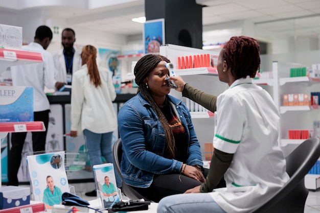 African american pharmacist measuring patient body temperature with non contact infrared thermometer. Drugstore medical check up, chemist using measurement instrument, all black team