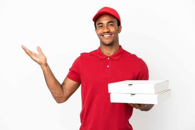 African American pizza delivery man picking up pizza boxes over isolated white wall extending hands to the side for inviting to come