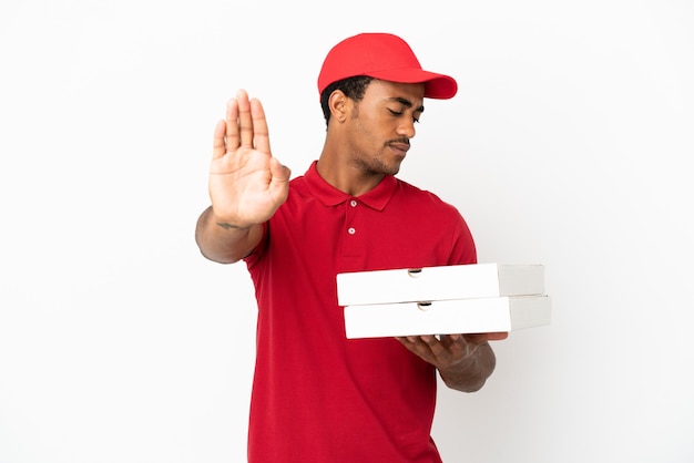 Афро-американский доставщик пиццы собирает коробки для пиццы над изолированной белой стеной, делая жест стоп и разочарованный