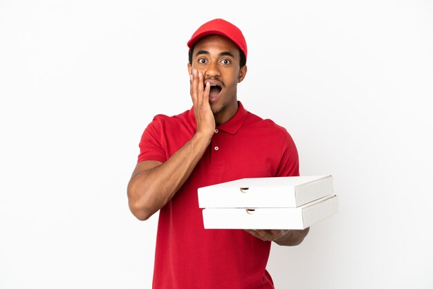 Uomo afroamericano di consegna della pizza che prende le scatole della pizza sopra il muro bianco isolato con sorpresa e espressione facciale scioccata