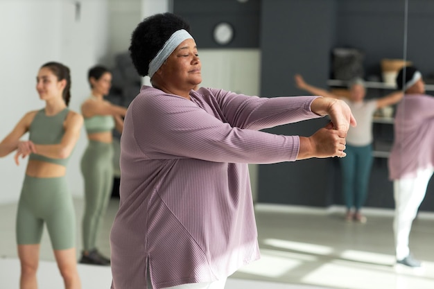 African american plump woman training in gym with other people in background