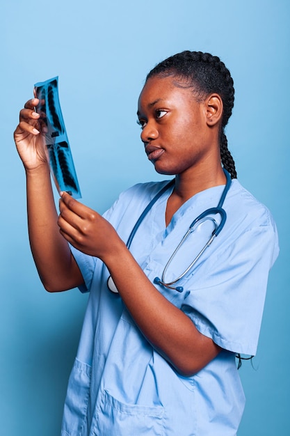 African american practitioner nurse holding radiography analyzing lungs expertise working at sickness treatment in studio with blue background. Therapist woman in medical uniform. Medicine concept