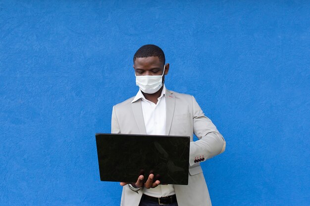 Afroamericano in una maschera protettiva con un laptop in mano