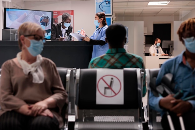 아프리카계 미국인 접수원은 병원 로비의 리셉션 데스크에서 아시아 간호사와 이야기를 나누며 의료 서비스와 진료 예약에 대해 이야기를 나눴습니다. 코비드 19 전염병 동안 시설 직원.