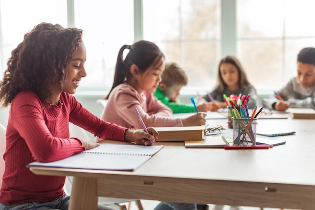 Apprendimento di scrittura della ragazza della scuola dell'afroamericano che si siede in aula