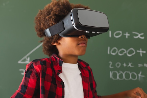 VR ヘッドセットを使用して教室の黒板の前でアフリカ系アメリカ人の男子生徒