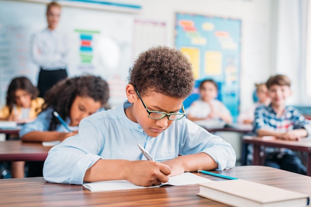 Photo african american schoolboy writing in notebook at school