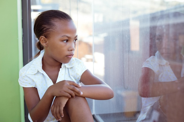 창 밖을 내다보는 학교 교실에 앉아 있는 아프리카 계 미국인 여학생