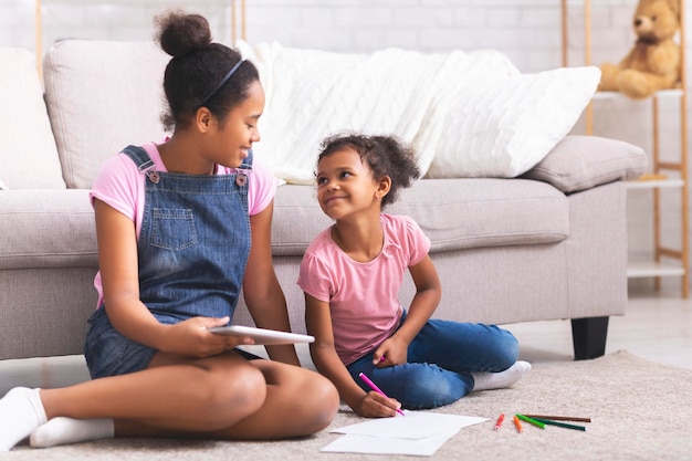 African american sisters drawing with colorful pencils on floor