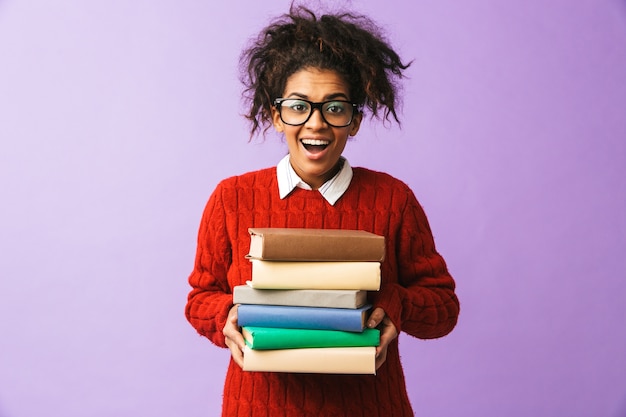 Афро-американская улыбающаяся девушка в школьной форме, держащая кучу книг, изолированные
