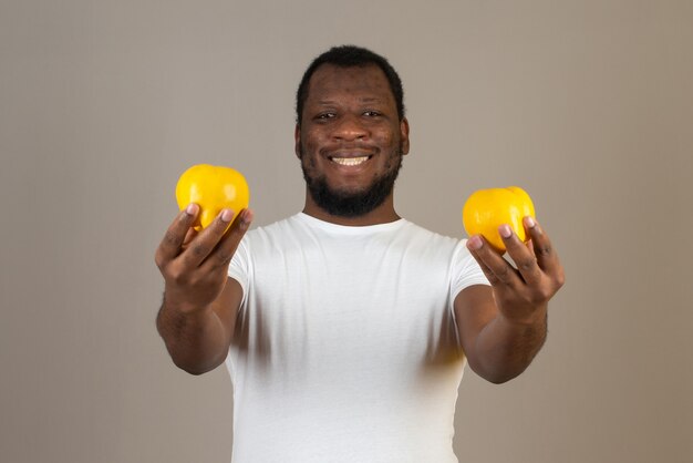 Uomo sorridente afroamericano con una mela cotogna in entrambe le mani, in piedi davanti al muro grigio.