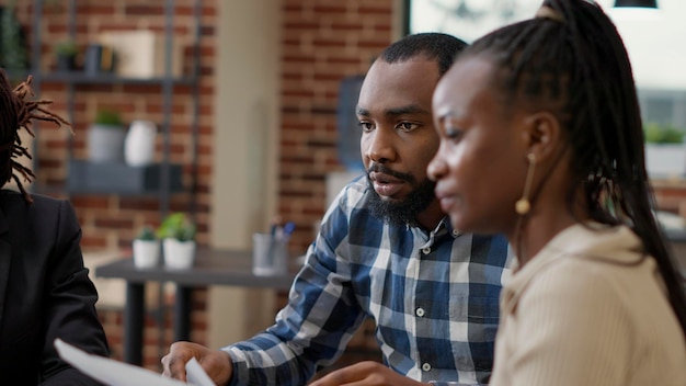 African american startup team working with statistics papers on project collaboration, using financial charts on documents to create analysis. Colleagues looking at graphs. Close up. Handheld shot.