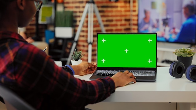 African american student analyzing greenscreen on laptop at\
desk, working with isolated display and mockup template on wireless\
pc. using portable computer with blank copyspace.