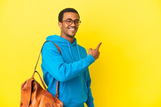 African American student man over isolated yellow background pointing back