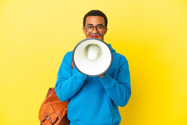 Афро-американский студент человек на изолированном желтом фоне кричит в мегафон