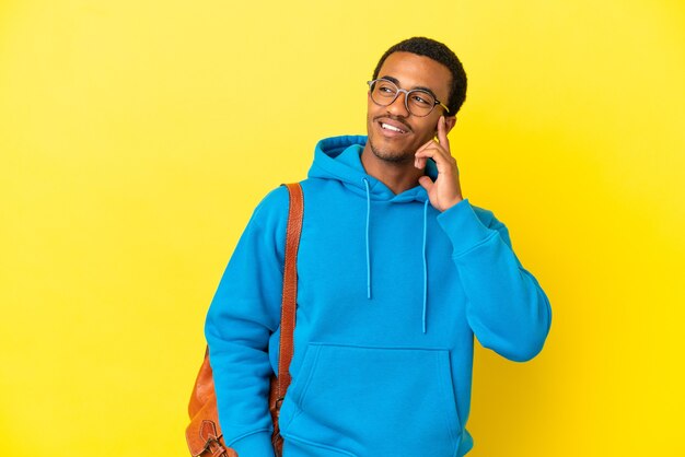 Афро-американский студент человек на изолированном желтом фоне думает о идее, глядя вверх