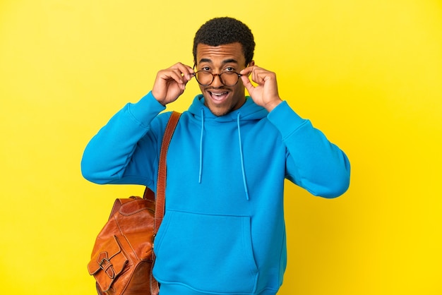 African American student man over isolated yellow background with glasses and surprised