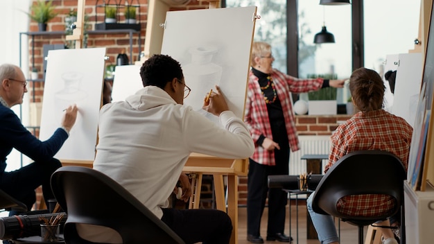 アフリカ系アメリカ人の学生が鉛筆を使ってキャンバスに花瓶のスケッチを描き、アート ワークショップに参加します。自己啓発のための描画スキルを学ぶ芸術クラスのレッスン。新年の抱負