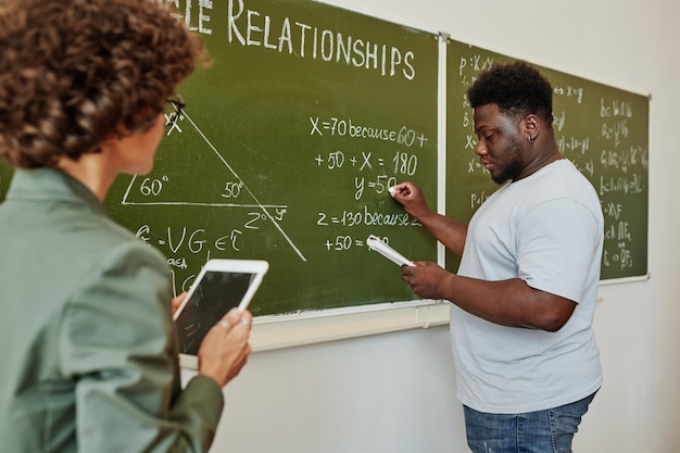 African american student writing down algebraic equation on blackboard