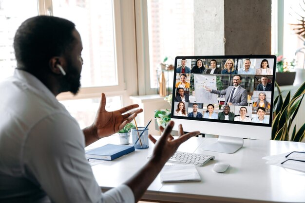 Foto uomo afroamericano di successo ceo manager consulente che tiene una conferenza aziendale online con dipendenti multirazziali seduti alla loro scrivania a casa gestando le mani discutere sulla strategia