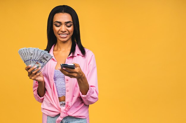 African american successful woman holding lots of money dollar banknotes and using mobile phone