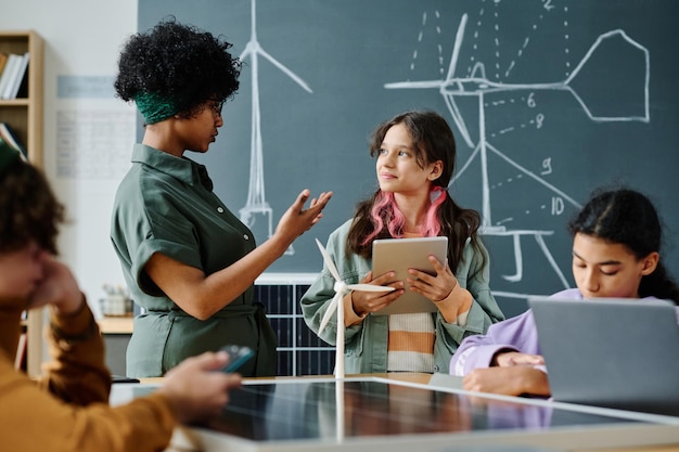 Photo african american teacher talking to students at lesson while they using gadgets