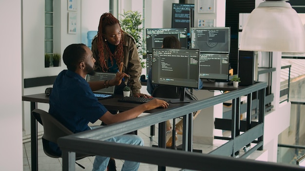 African american team of developers talking about source code running on screen, analyzing server information. Database admins collaborating on data coding project in ai programming room.