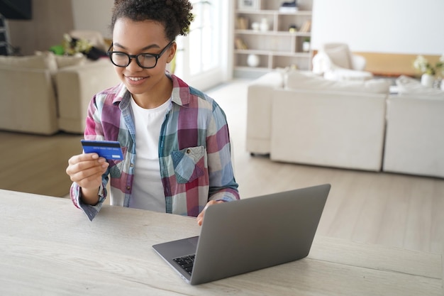 African american teen girl holds banking credit card shopping online at laptop at home E commerce