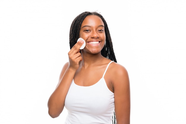 African American teenager girl with long braided hair removing makeup from her face with cotton pad