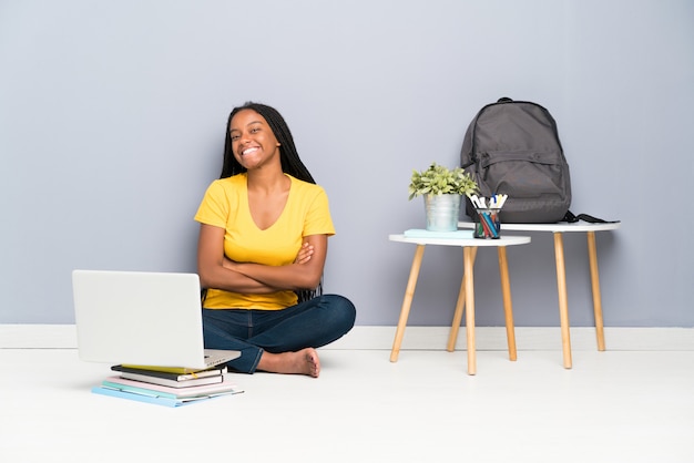 African American teenager student girl with long braided hair sitting on the floor laughing