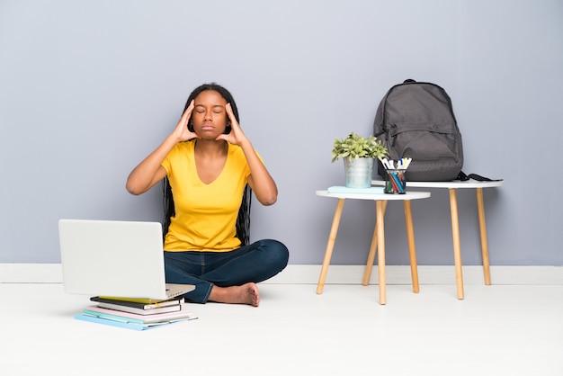 African American teenager student girl with long braided hair sitting on the floor unhappy and frustrated 