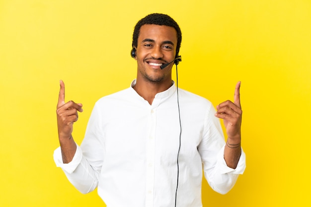 African American Telemarketer man working with a headset over isolated yellow background pointing up a great idea