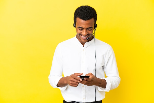 African American Telemarketer man working with a headset over isolated yellow background sending a message with the mobile