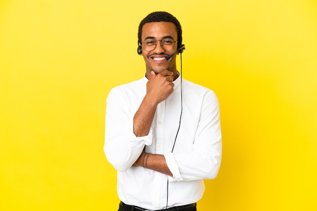 African American Telemarketer man working with a headset over isolated yellow background with glasses and happy
